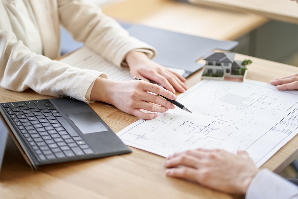 Image of two people discussing a floor plan, with a laptop and a miniature house in the background, representing property development.